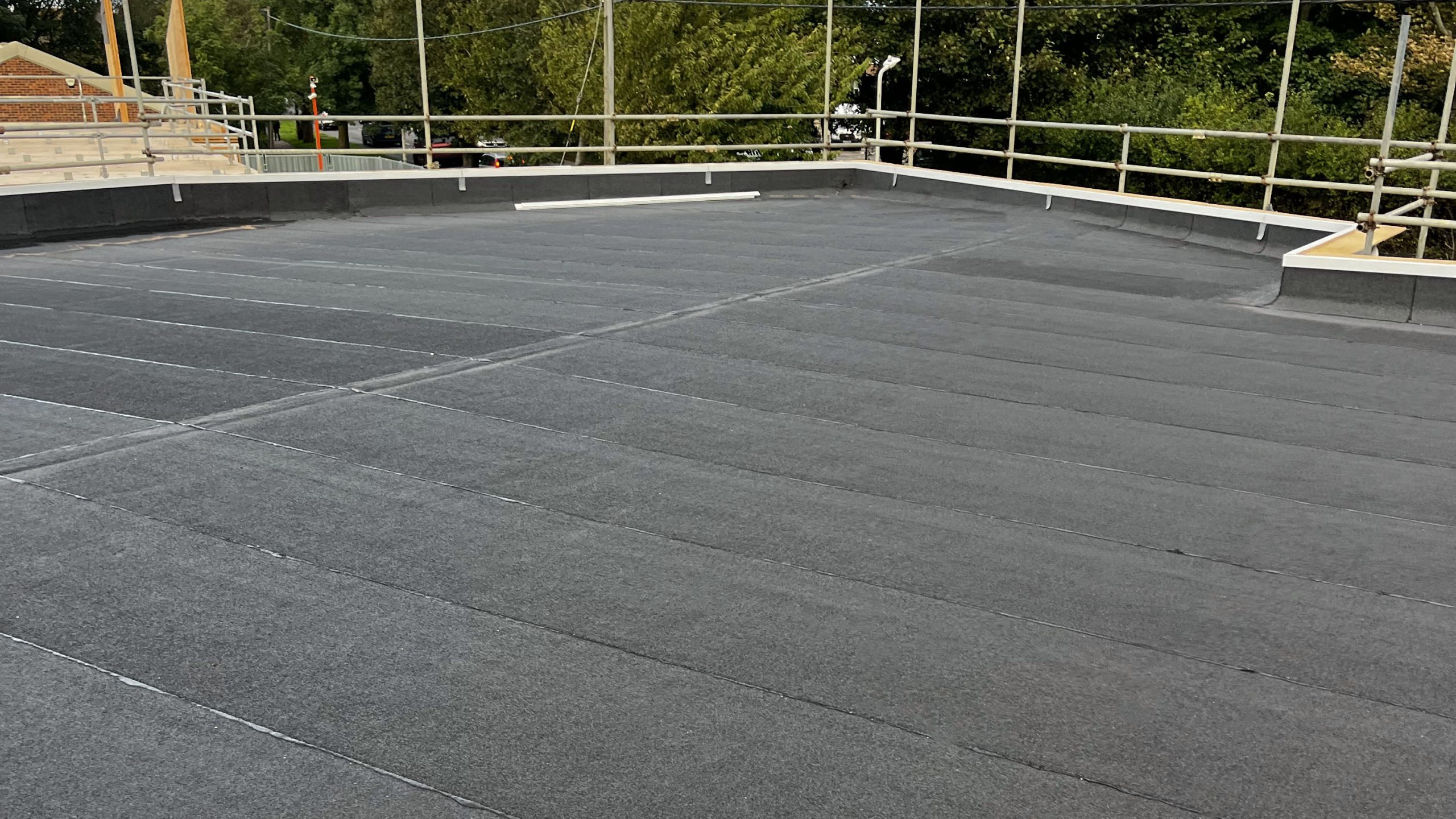 Felt roofing South East – torch-on felt system installed on a flat commercial roof with edge protection